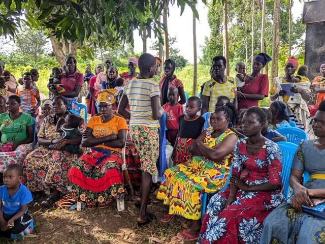 Women seated together under a tree at a savings meeting